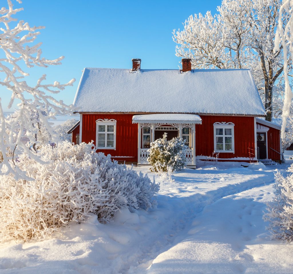 Idyllisk röd stuga med en vinter trädgård Stuga i snö